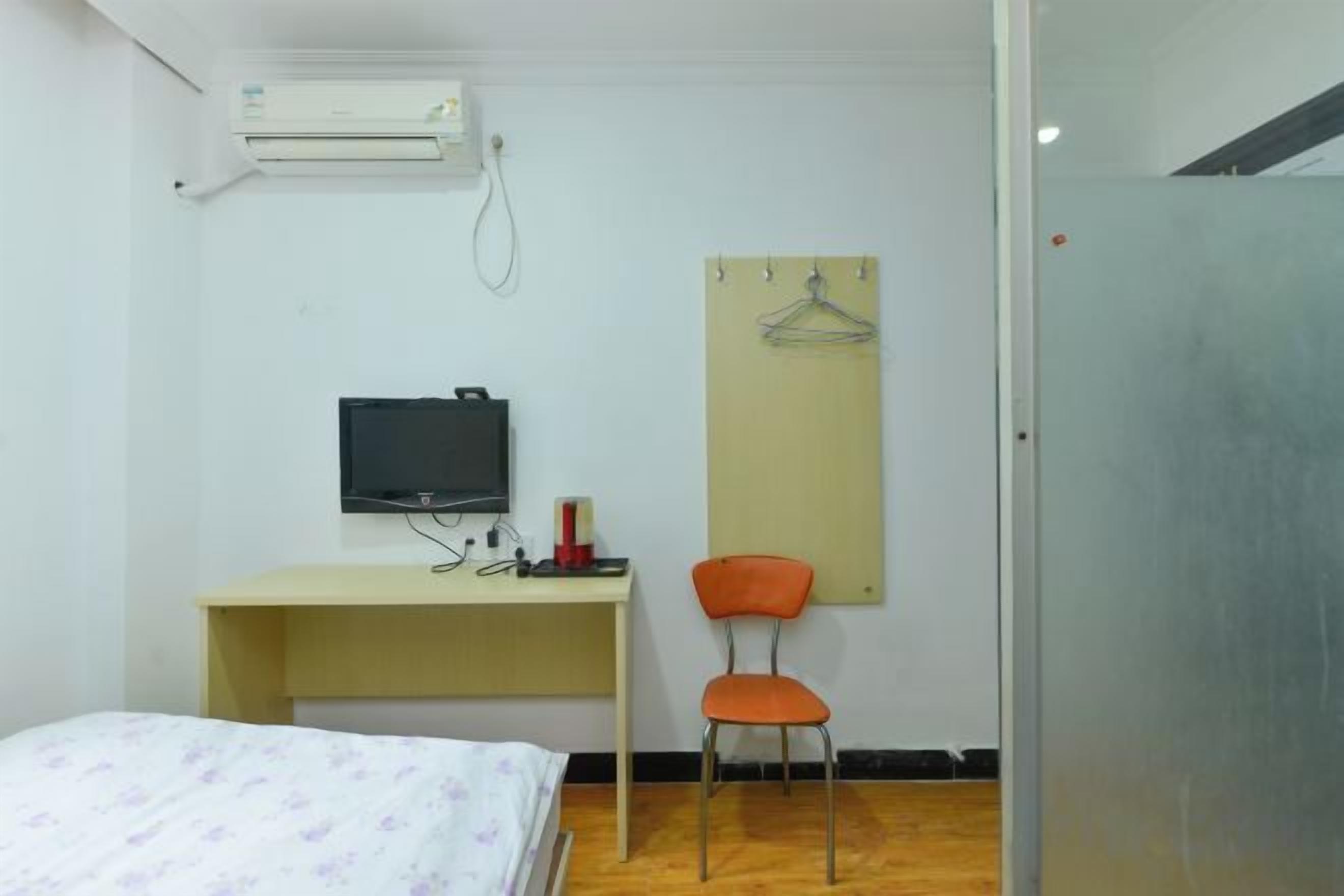 A room with a bed, a desk with a computer, a chair, and a wall-mounted TV.
