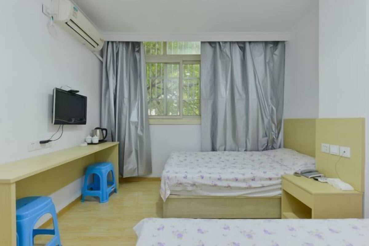 Une chambre avec un lit, un bureau, une télévision et une fenêtre avec des rideaux.