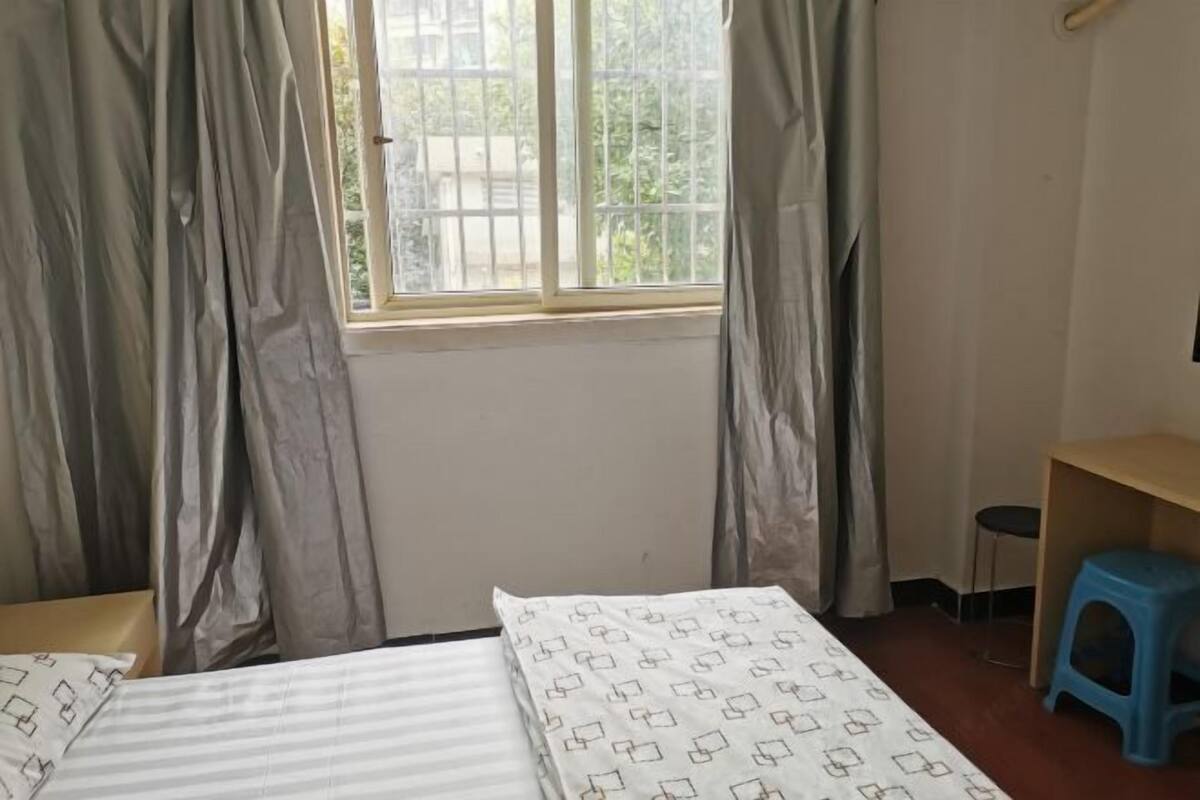 Une chambre avec deux lits, une fenêtre avec des rideaux, un petit tabouret et une étagère en bois.