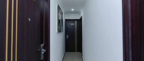 A narrow hallway with a wooden door on the left and a dark door at the end.