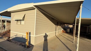 A building with a covered patio area, a small window, and a shadow of a person. - 2-bedroom mobile home in enchanting Havasu Lake with WiFi, AC (Havasu Lake)