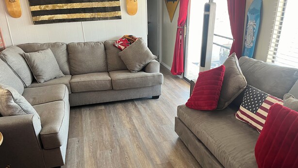 A living room with a sectional sofa, a smaller armchair, and a red and black American flag pillow. - 2-bedroom mobile home in enchanting Havasu Lake with WiFi, AC (Havasu Lake)
