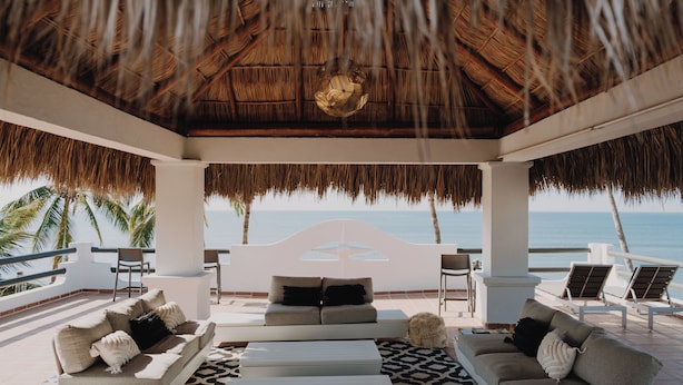 A beachside lounge with a thatched roof, white sofas, and a view of the ocean. - Villa Cobojo (Bucerías)