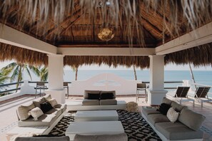 A beachside lounge with a thatched roof, white sofas, and a view of the ocean. - Villa Cobojo (Bucerías)