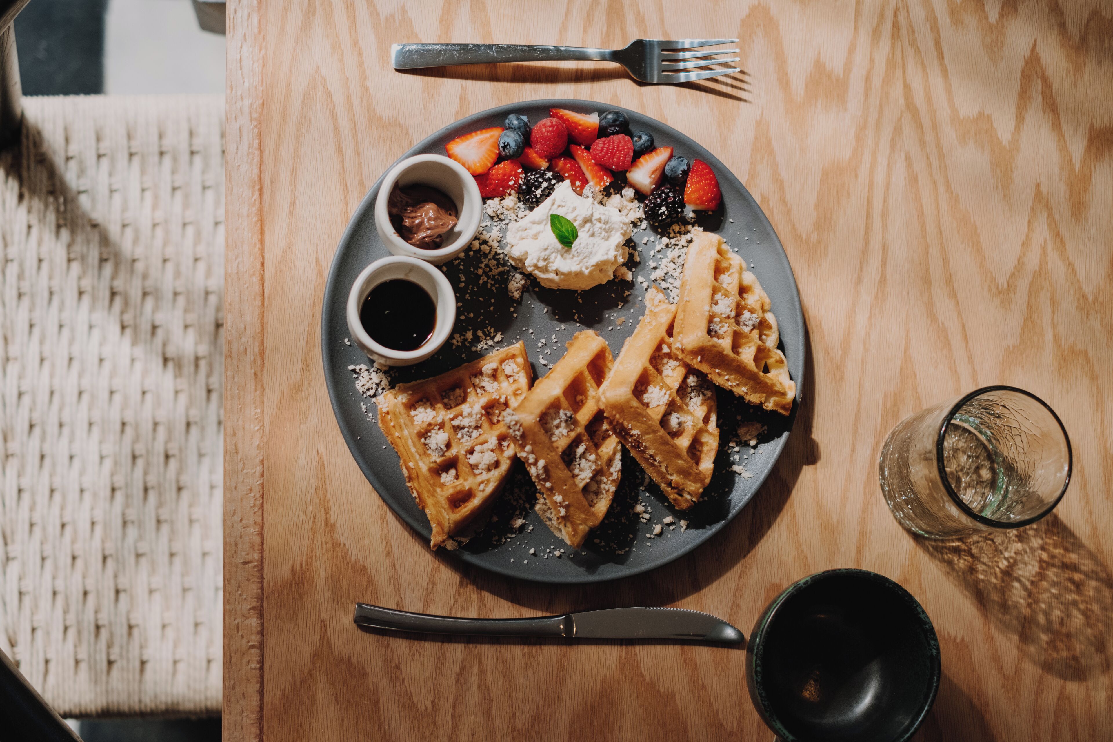 A plate of waffles with fruit and whipped cream on a wooden table.