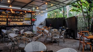 An outdoor seating area with wicker chairs and tables, a bar with shelves of bottles, and a view of lush greenery. - Villa Cobojo (Bucerías)