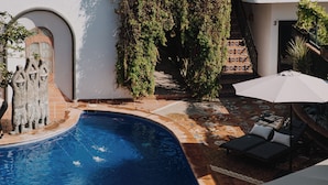A swimming pool with a tiled deck, a stone sculpture, and a lounge area with a white umbrella. - Villa Cobojo (Bucerías)