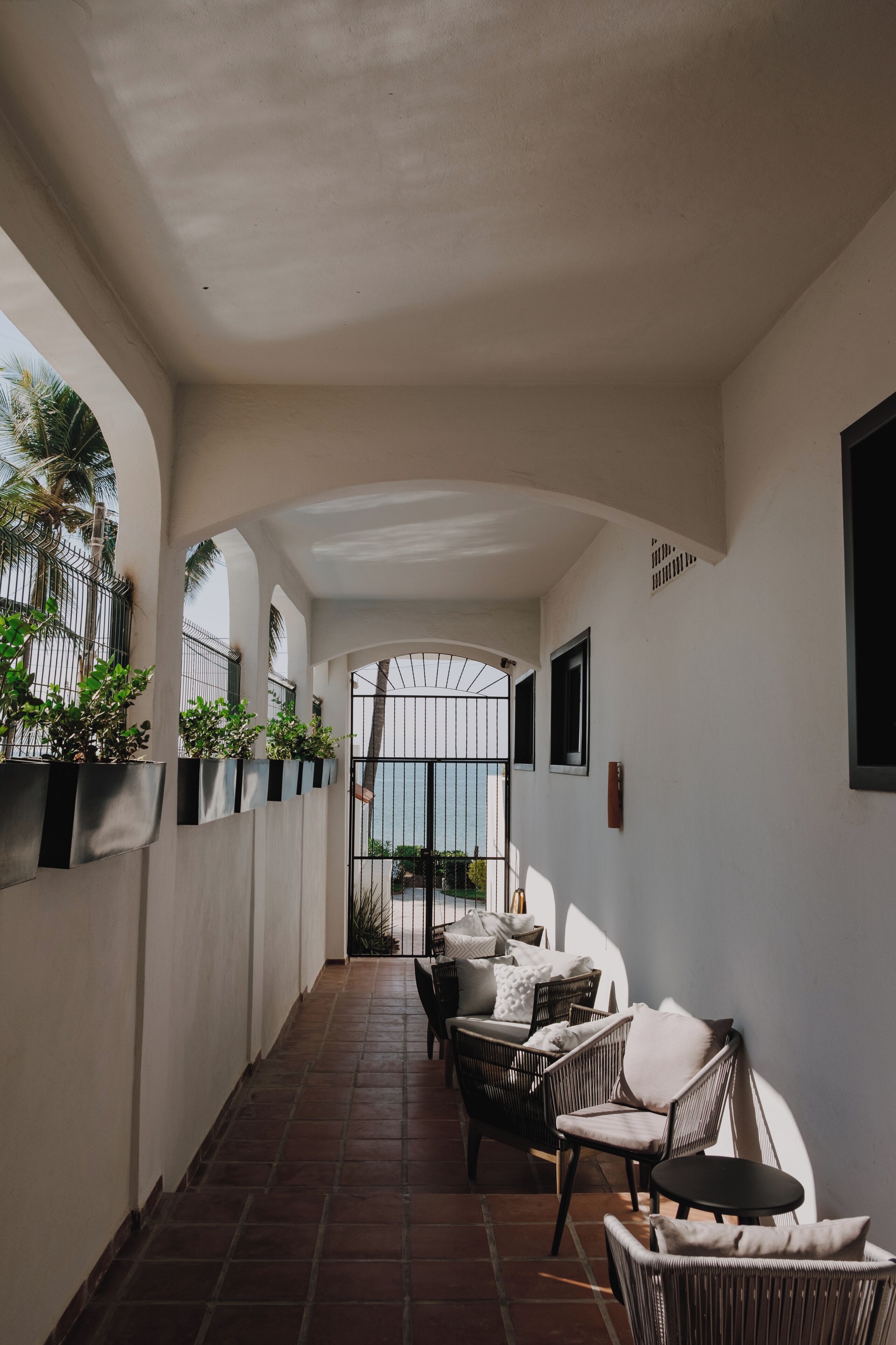 A corridor with a tiled floor, wicker furniture, and potted plants.