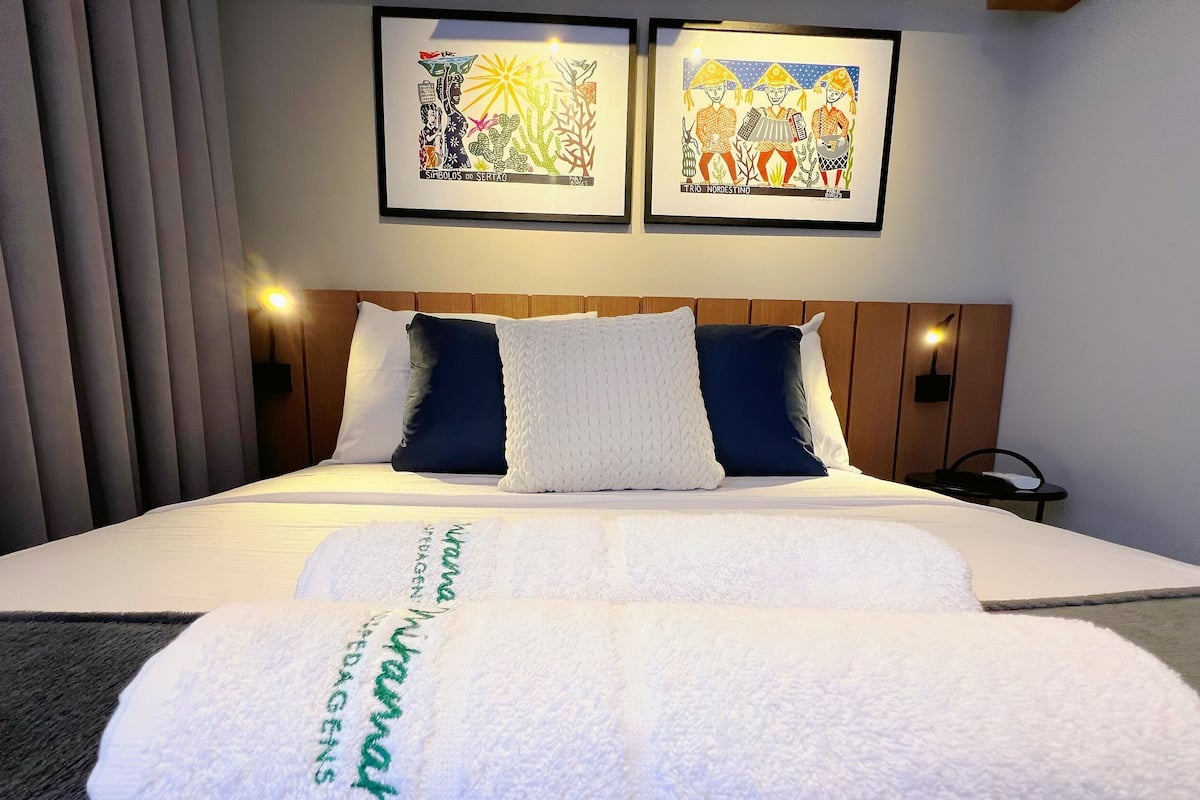 A hotel room with a bed, two framed artworks on the wall, a bedside table, and a nightstand.
