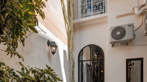 A courtyard with a table and chair, a potted plant, and a door with a wrought iron gate. - Modern Designer 2BR Apartment – Walk to Sea (Sliema)