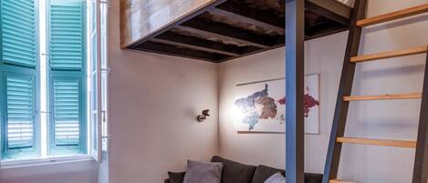 A cozy room with a wooden dining table, a sofa, a chandelier, and a ladder against the wall.