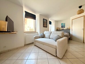 A living room with a sofa, a television, a window with a view, and a door leading to another room.