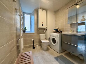 A compact bathroom with a toilet, washing machine, and a small window.