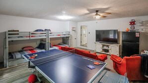 A room with bunk beds, a ping pong table, a television, and a refrigerator.