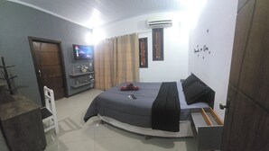 A bedroom with a bed, a TV, a wardrobe, and a small table with a chair. - MARINAS DUPLEX HOUSE (Marinas Angra dos Reis)