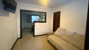 A small, well-lit room with a bed, a desk with a chair, and a TV mounted on the wall. - MARINAS DUPLEX HOUSE (Marinas Angra dos Reis)