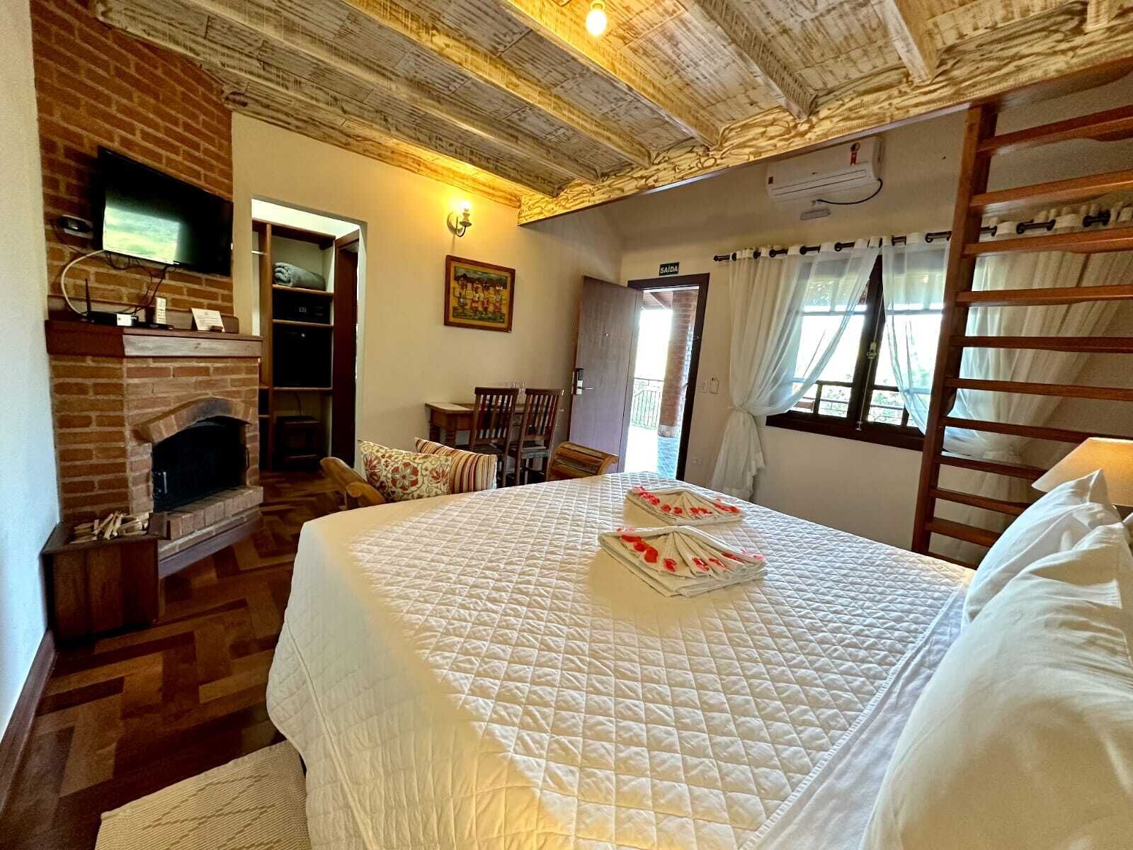 A cozy room with a brick fireplace, a bed with a quilt, a wooden ladder, and a television mounted on the wall.