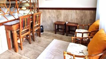 A room with a wooden dining table, two chairs, a sofa with cushions, a patterned rug, and two wall-mounted paintings.