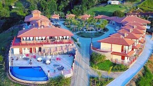 A resort with multiple buildings, a swimming pool, and a landscaped area with palm trees. - Aldeia Manacás Pousada Conceito (São Bento do Sapucaí)