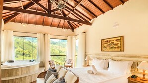 A bedroom with a large bed, a chaise lounge, a wooden ceiling, and a view of green hills. - Aldeia Manacás Pousada Conceito (São Bento do Sapucaí)