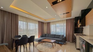Una sala de estar moderna con sofá, mesa de comedor, sillas y una zona de cocina con estufa y lavadora.