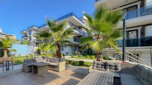 Un área de lounge al aire libre moderna con mobiliario de mimbre, palmeras y una piscina al fondo.