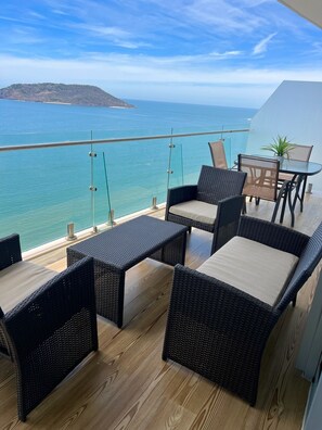 Enjoy the ocean view from this balcony with wicker furniture and a potted plant.