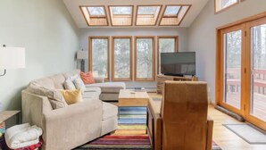 A modern living room with a sofa, armchair, TV, and large windows. - Spacious 4-bedroom house in fabulous Parksville perfect for Spring escape (Parksville)