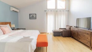 A bedroom with a bed, a bench, a TV, a dresser, and a window with curtains. - Spacious 4-bedroom house in fabulous Parksville perfect for Spring escape (Parksville)