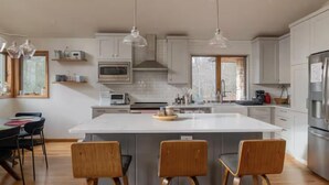 A modern kitchen with white cabinets, a central island with bar stools, a microwave, and a stainless steel refrigerator. - Spacious 4-bedroom house in fabulous Parksville perfect for Spring escape (Parksville)