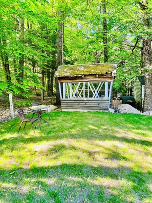 A rustic wooden cabin with a porch, surrounded by a fenced yard and dense trees. - Cozy Cottage on a Lake, near Gunstock Mountain (Gilmanton)