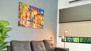 En moderne stue med en hjørnesofa, et farverigt billede, en aircondition og en gulvlampe.