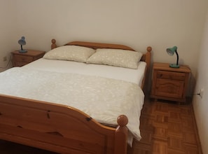 Ein hölzernes Bett mit weißer Bettdecke und zwei Kissen, flankiert von zwei Nachttischen mit Lampen.