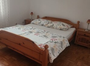 Uma cama de madeira com colcha e almofadas florais, ladeada por mesas de cabeceira com abajures.