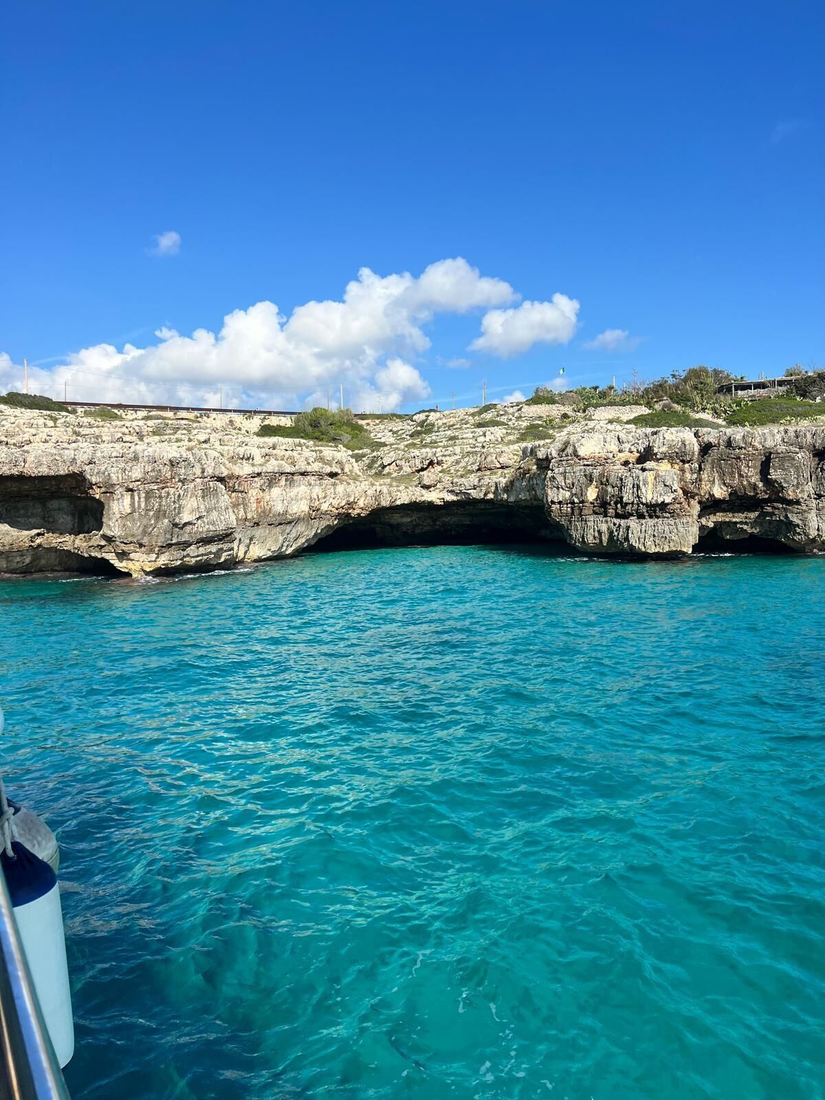 Eine felsige Küstenlandschaft mit klarem, türkisblauem Wasser und einer sichtbaren Brücke.