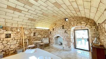 Une chambre aux murs de pierre, avec un lit, une petite table, une chaise, une cheminée et une vue sur l’extérieur.