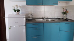 A modern kitchen with teal cabinets, a white refrigerator, and a stainless steel sink. - Metajna House - Two-Bedroom Apartment (A1) (Pag)