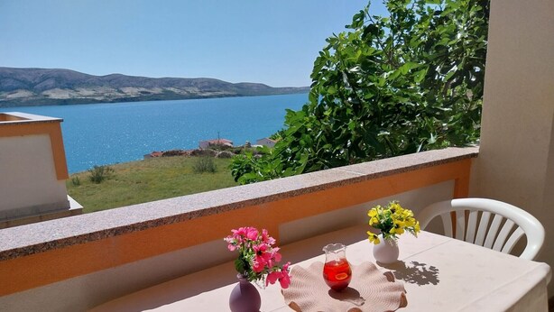A balcony with a table set for two, overlooking a body of water and hills. - Metajna House - Two-Bedroom Apartment (A1) (Pag)