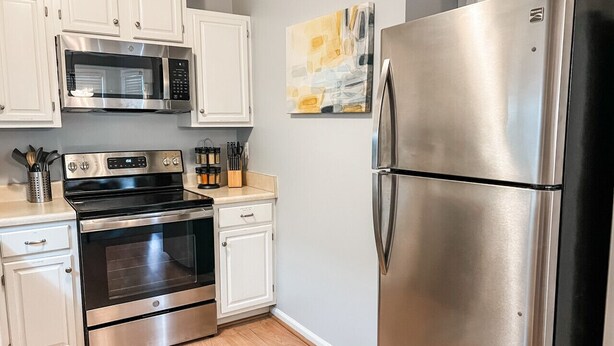 A modern kitchen with stainless steel appliances, white cabinetry, and a wooden floor. - Charming 2-Bedroom Townhome in Downtown Cary (Cary)
