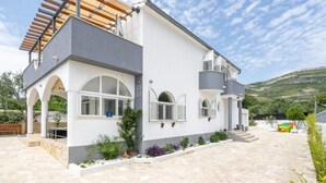 Una casa moderna de dos pisos con un patio empedrado de piedra, paredes blancas y detalles en gris.