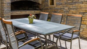 Une terrasse extérieure avec un mur en briques, une table en métal et quatre chaises.