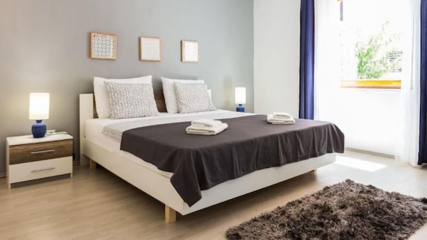 Une chambre moderne avec un grand lit, des tables de chevet et une vue sur la verdure par la fenêtre.