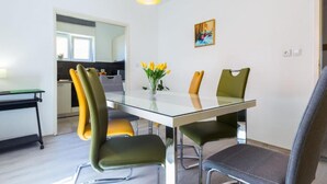 Un espace repas moderne avec une table en verre, des chaises vertes et jaunes, un vase rempli de fleurs jaunes et un tableau accroché au mur.