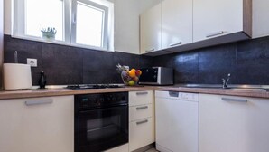 Une cuisine moderne avec des meubles blancs, un four noir, un lave-vaisselle et un panier de fruits posé sur le plan de travail.