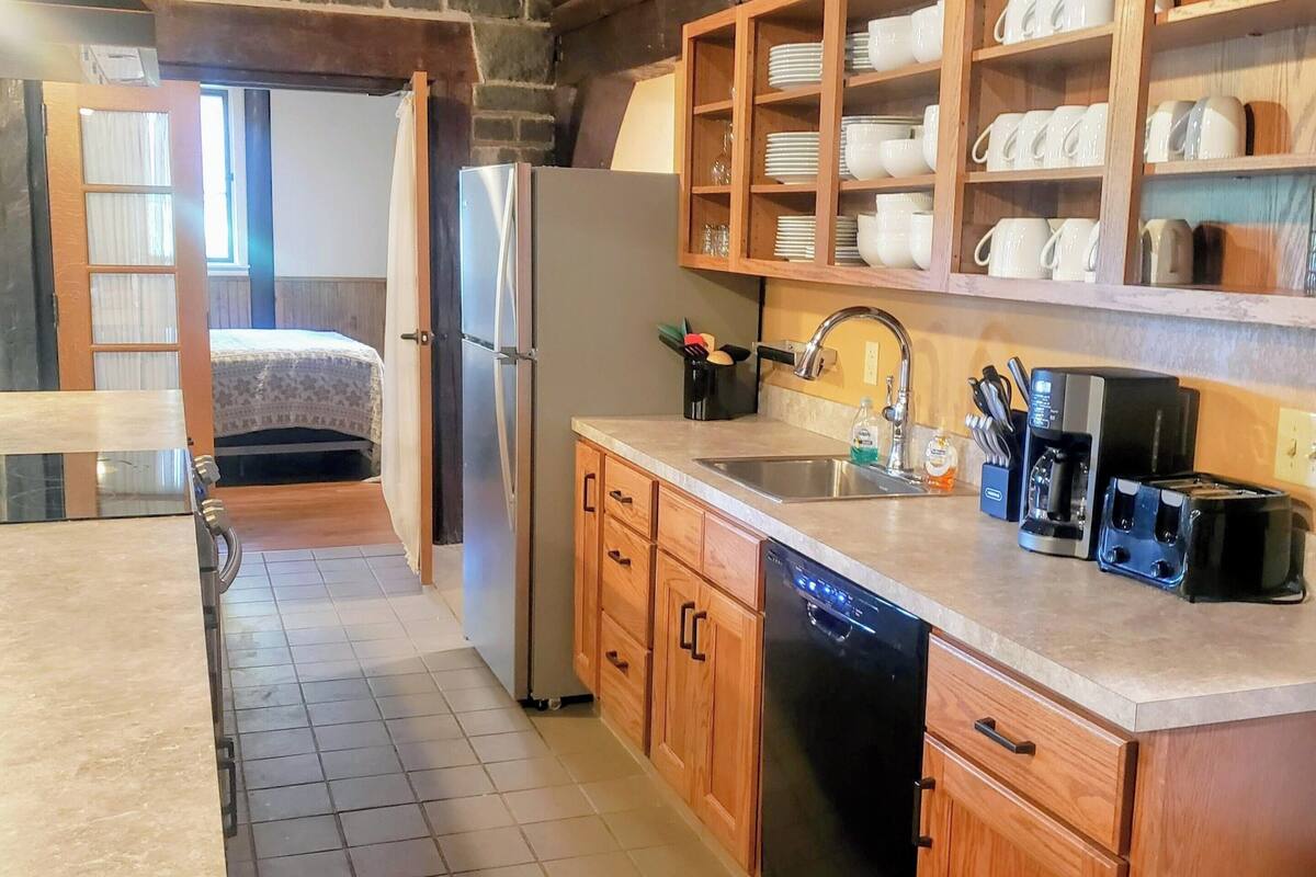A compact kitchen with wooden cabinets, a dishwasher, a refrigerator, and a coffee maker.