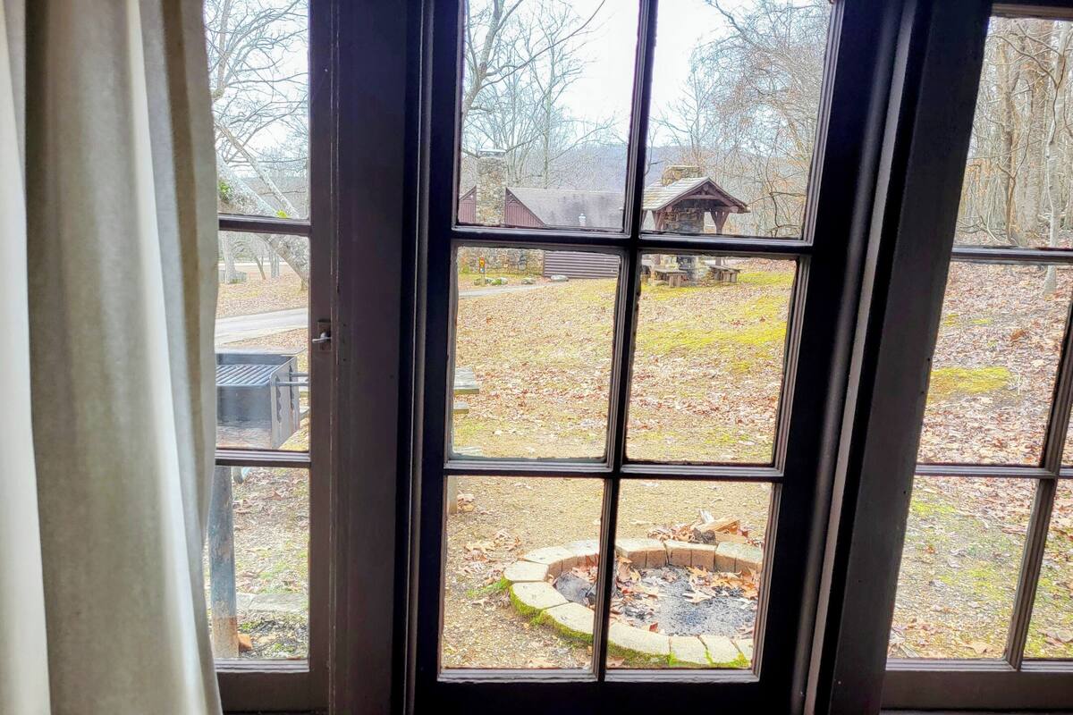 A view through a window with a stone wall and a wooden structure in the background.