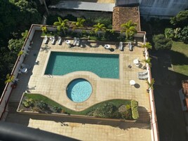 Vista aérea de uma piscina no terraço com uma banheira de hidromassagem circular, rodeada por espreguiçadeiras e palmeiras.