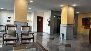 Egy előtér, melyben üveglapos asztal, fa székek, tűzoltó készülék, egy ajtó és egy hűtőszekrény található.