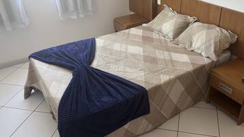 Una cama bien hecha con una colcha estampada y almohadas, una manta azul sobre el pie de la cama, y mesitas de noche de madera con cajones.
