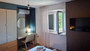 Un dormitorio con cama, escritorio, armario, televisor y ventana con vistas.